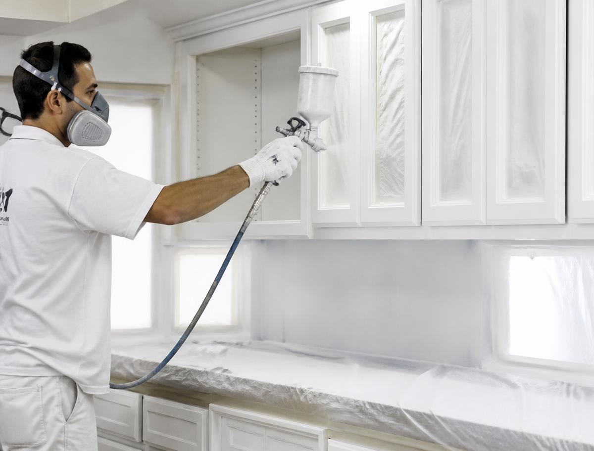 Painter spraying kitchen cabinets a fresh white finish